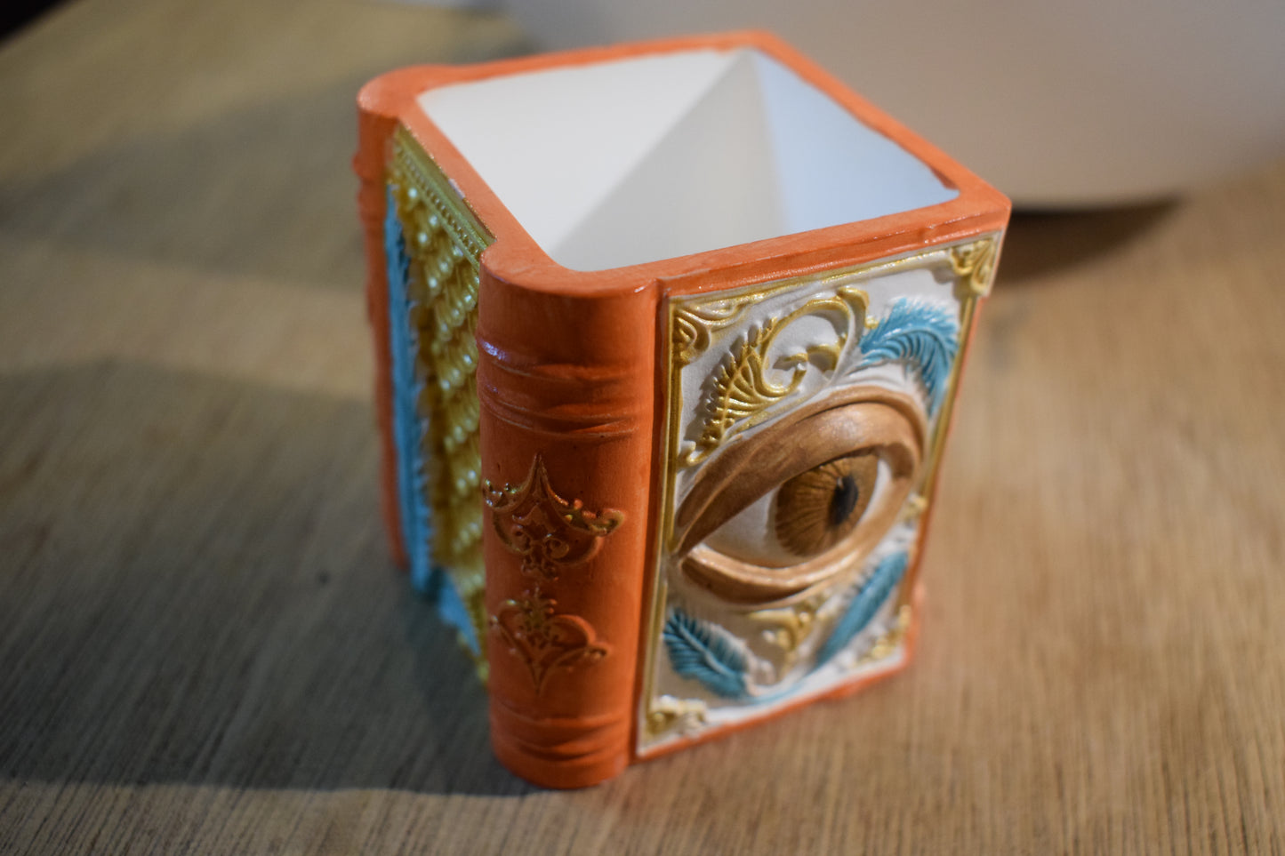 Pot en forme de livre oeil et plumes et volutes dorées