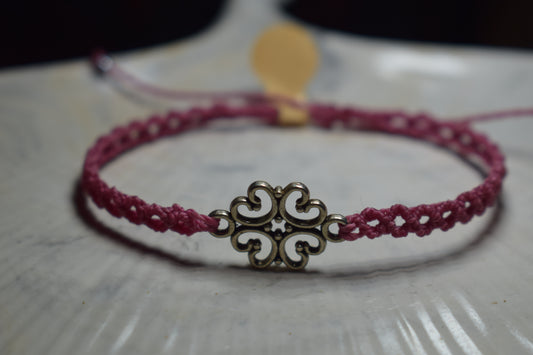 Bracelet en macramé rose avec un charm central en forme de trèfle stylisé